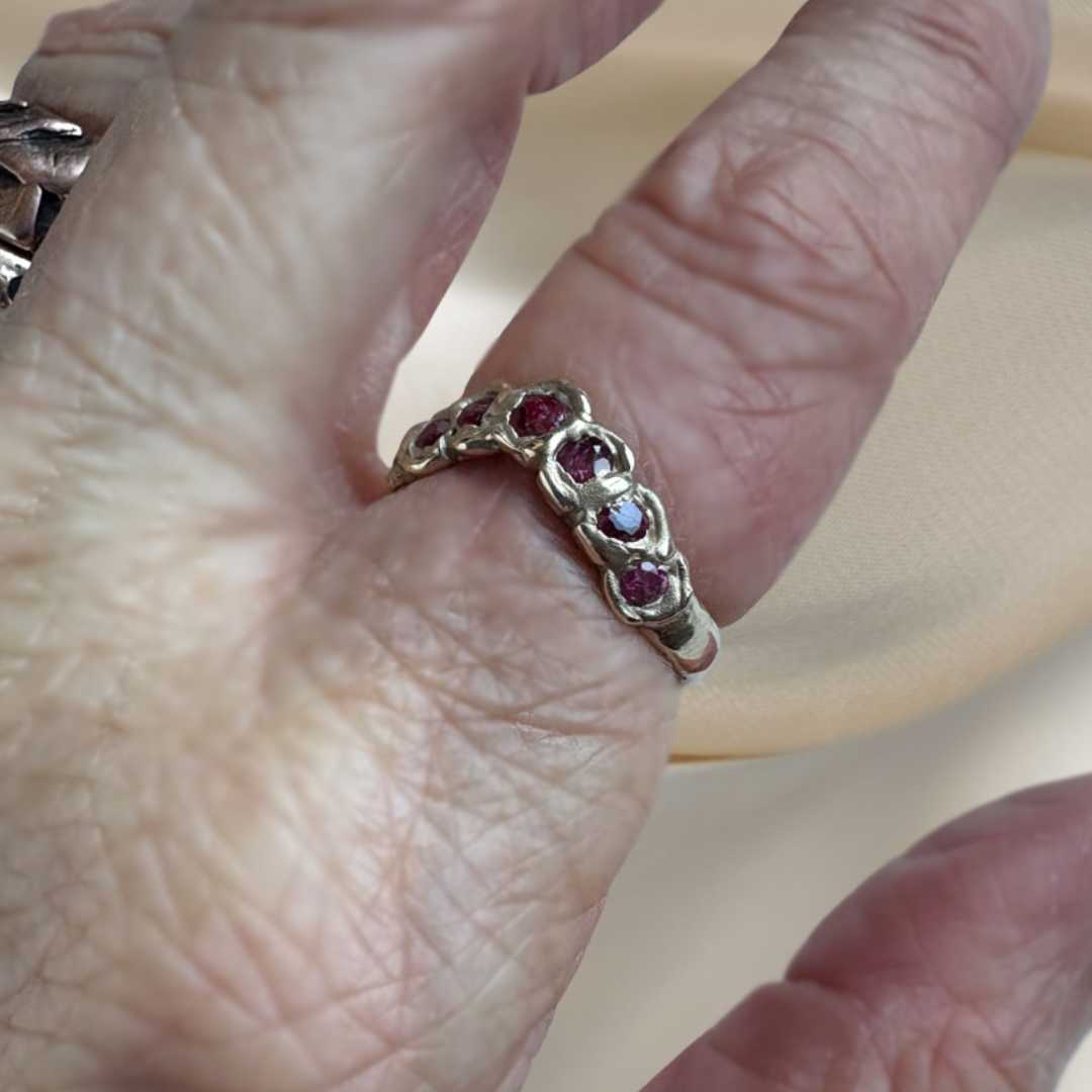 A close-up of a hand wearing a gold band ring set with five round-cut red gemstones.
