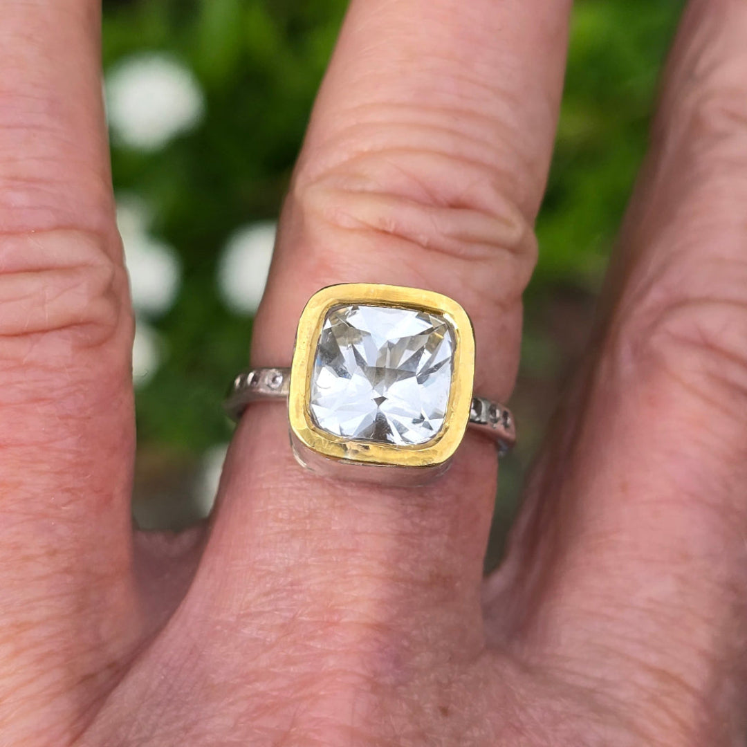 Gold and silver ring with a large topaz on a finger against a blurred green background