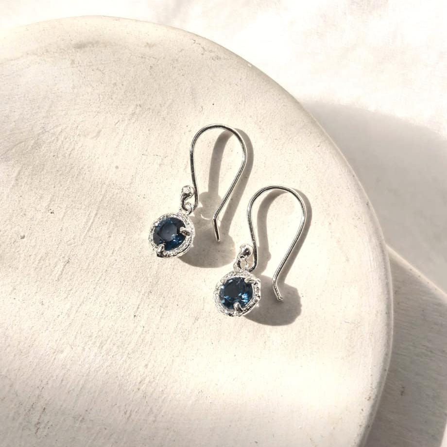 Silver earrings with blue gemstones on a white stone surface