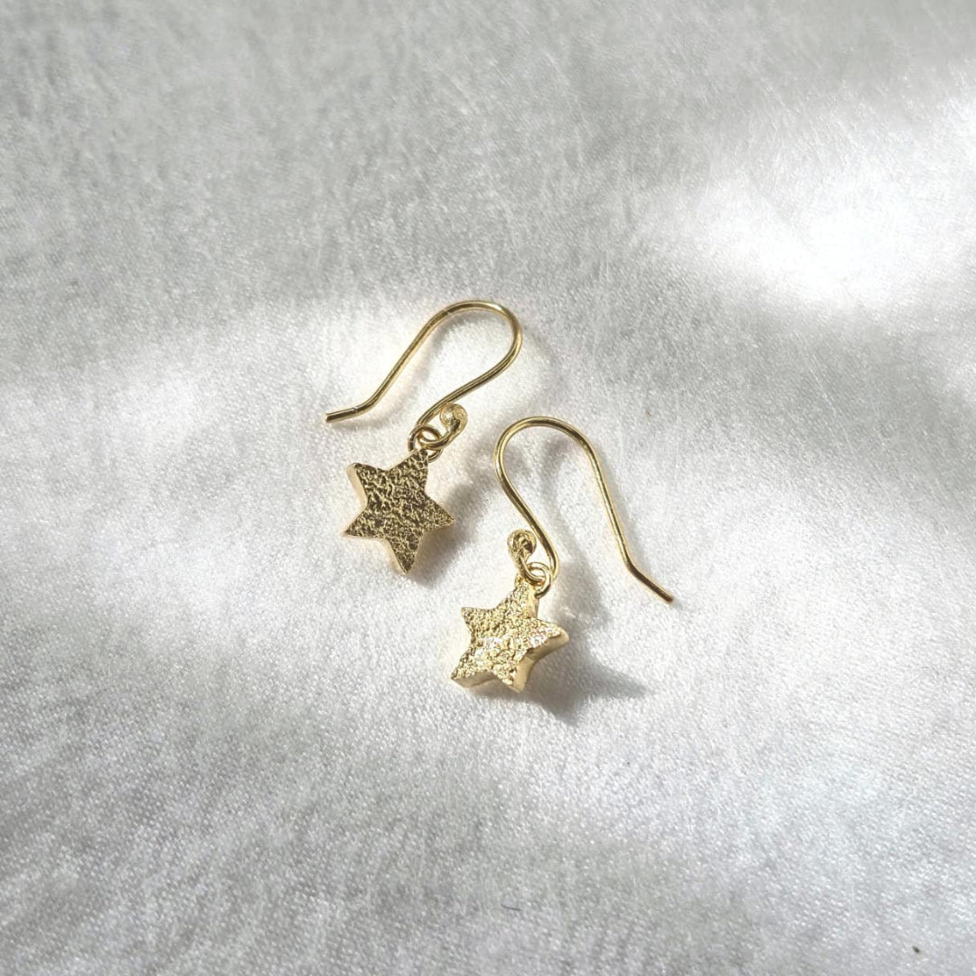 Gold star-shaped earrings on a silver background