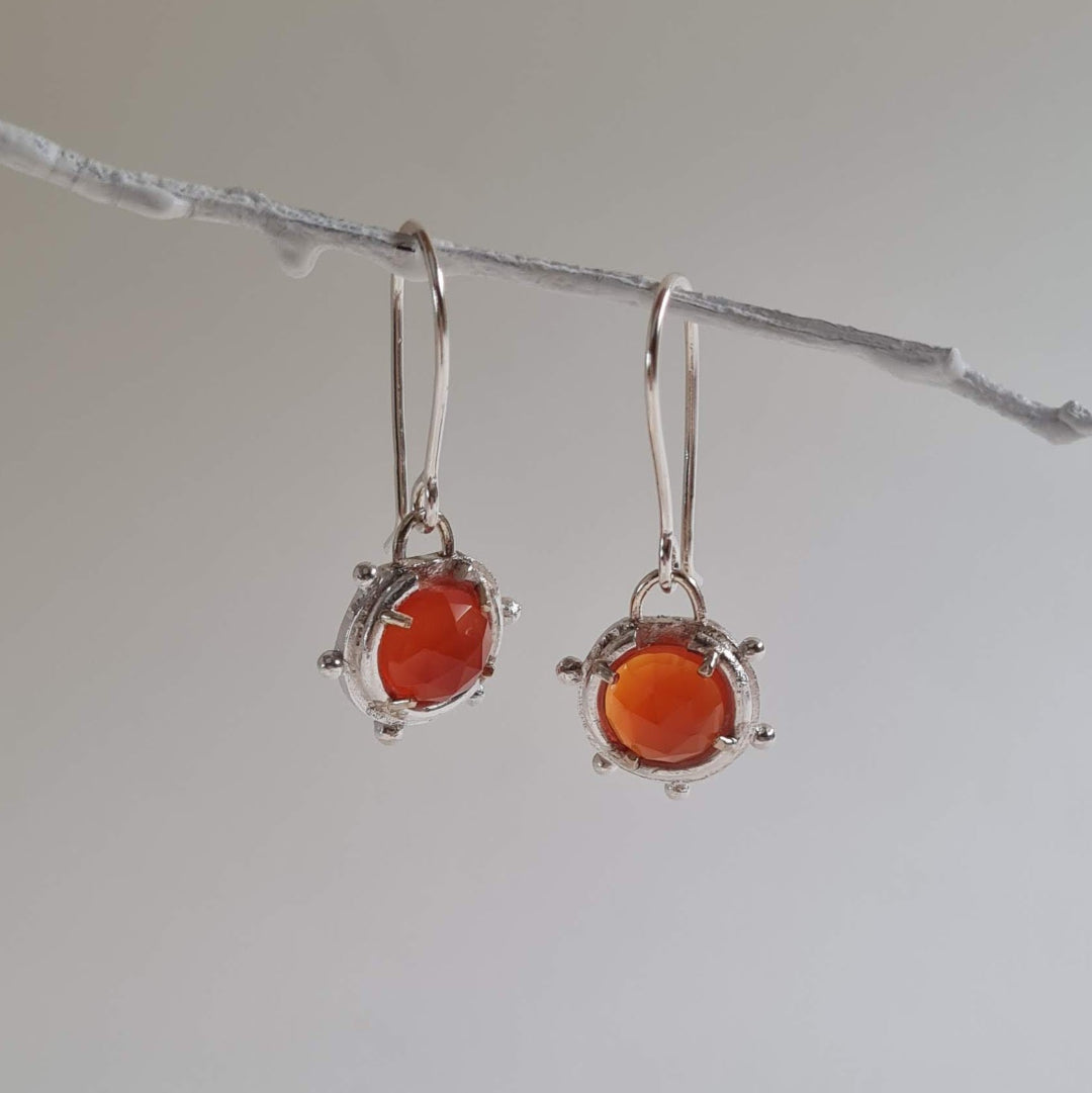Pair of silver earrings with orange gemstones hanging on a branch.
