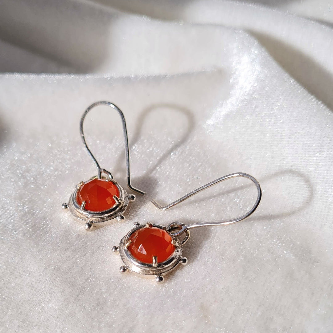 Silver earrings with orange stones on a white fabric background