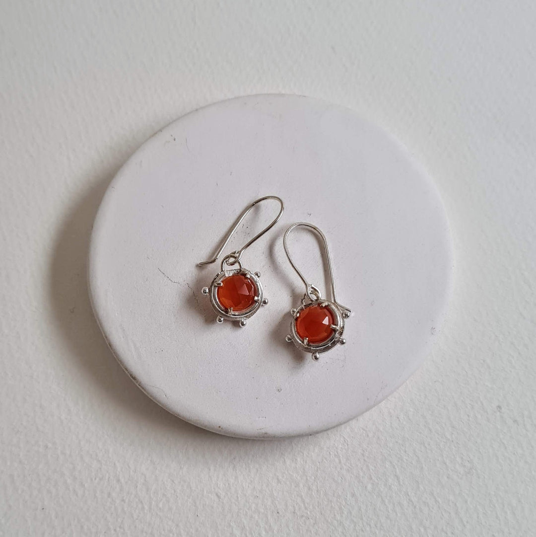 Silver earrings with orange stones on a white stone surface