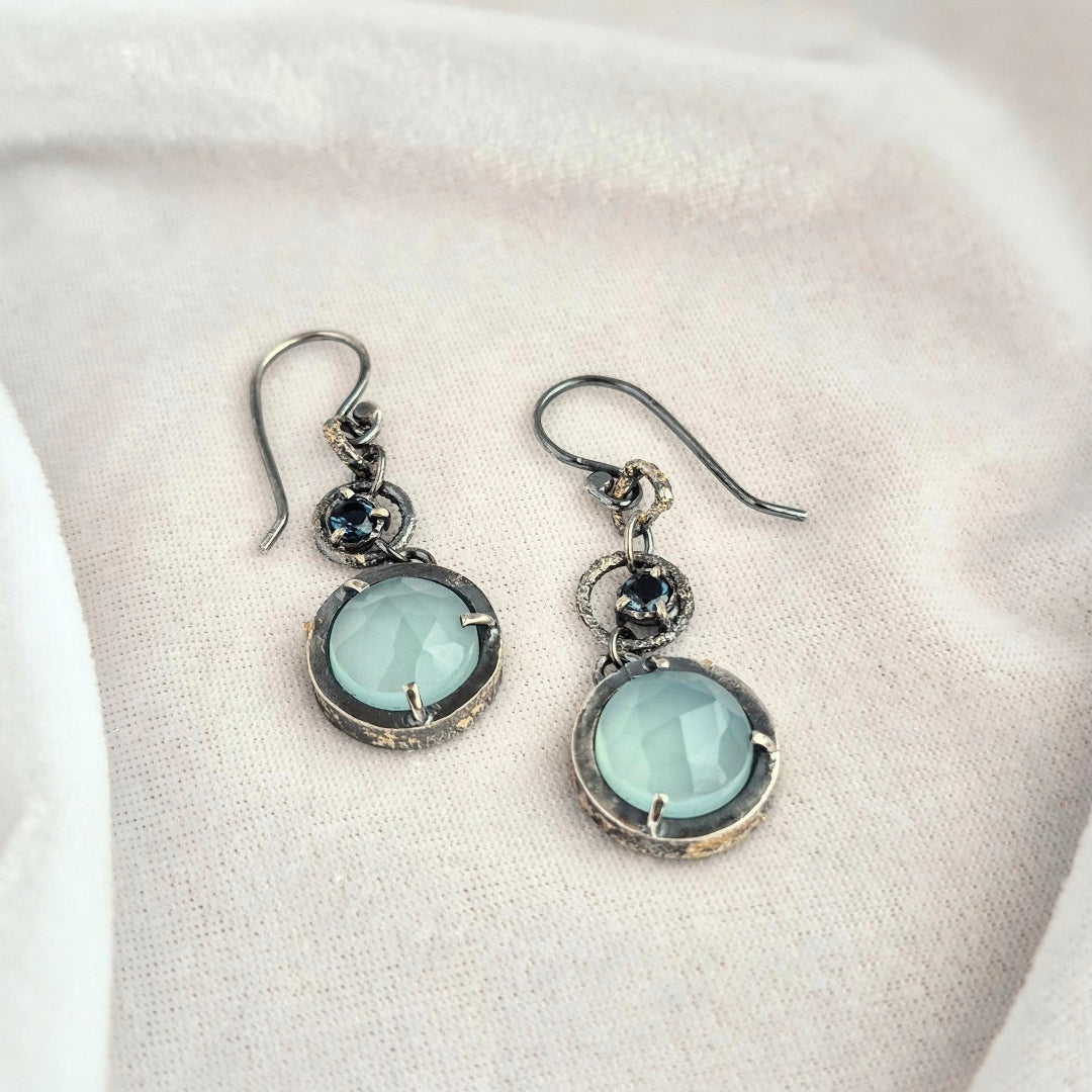 Pair of silver earrings with light blue gemstones on a white surface