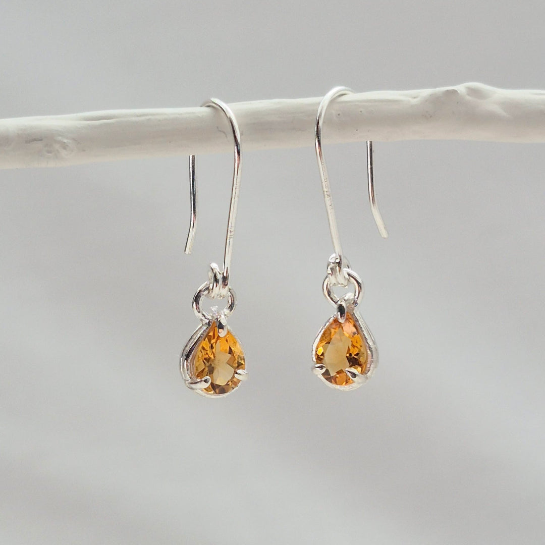Pair of teardrop-shaped citrine silver earrings on a white background