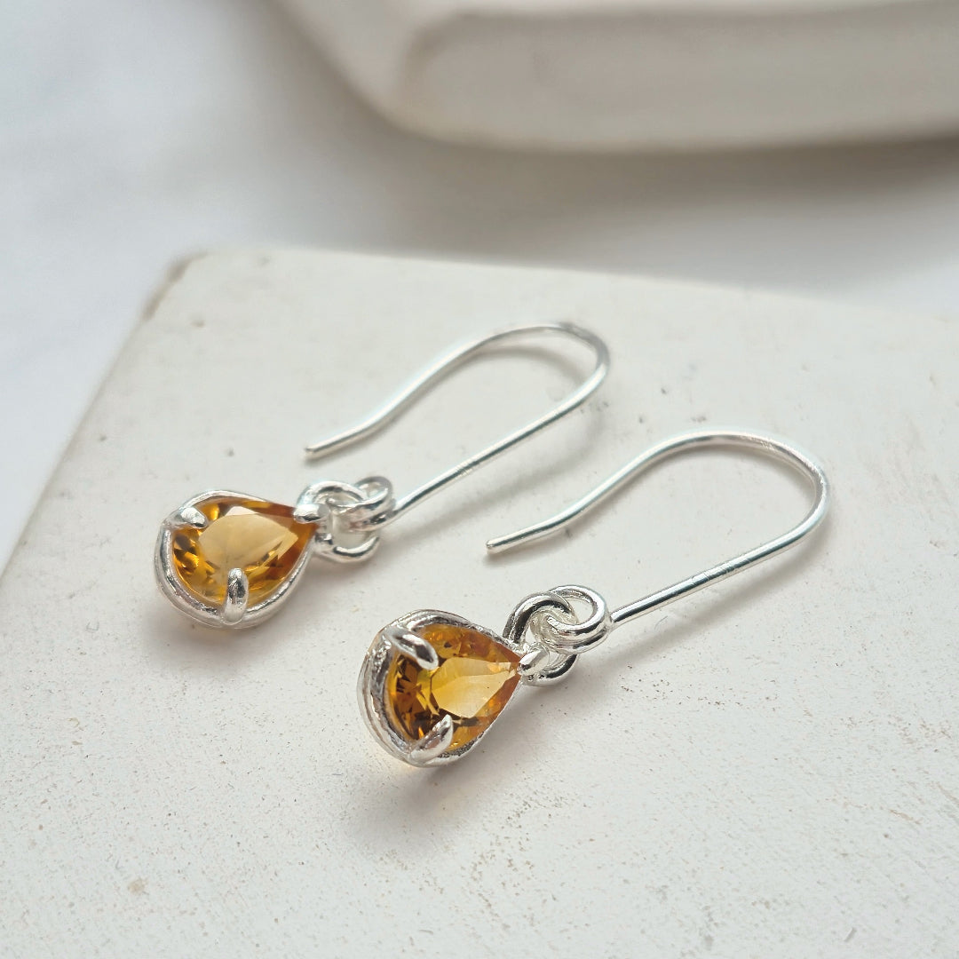 Silver earrings with teardrop-shaped citrine yellow gemstones on a light surface.