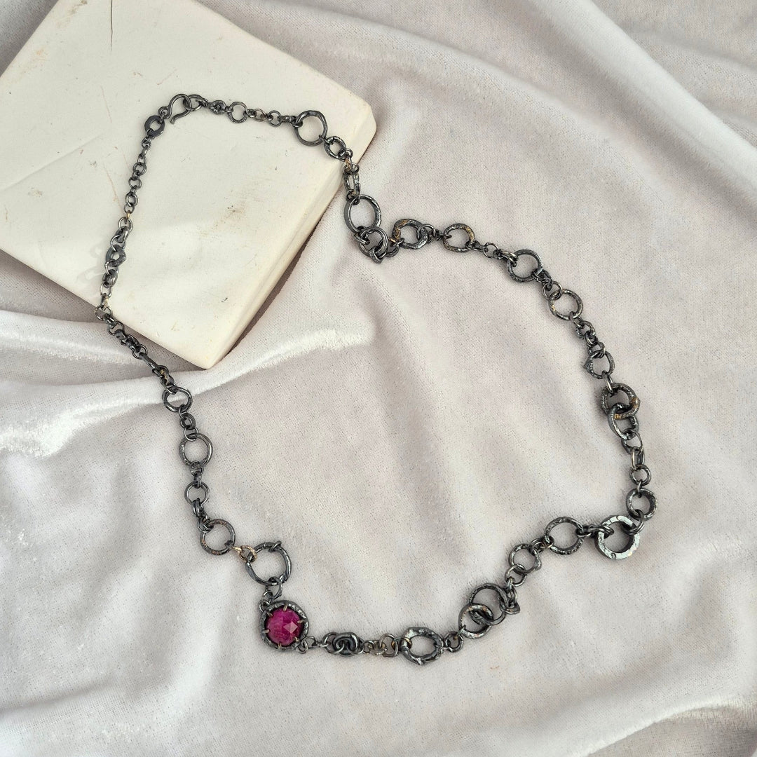 Oxidised silver chain necklace with a pink ruby on a white fabric background