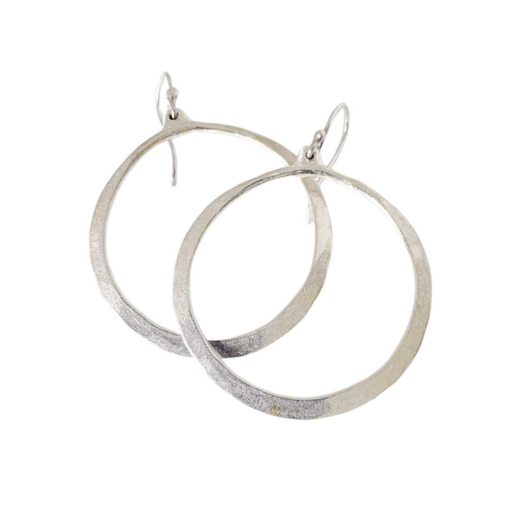 A pair of textured silver hoop earrings with fishhook backings, displayed against a solid white background.