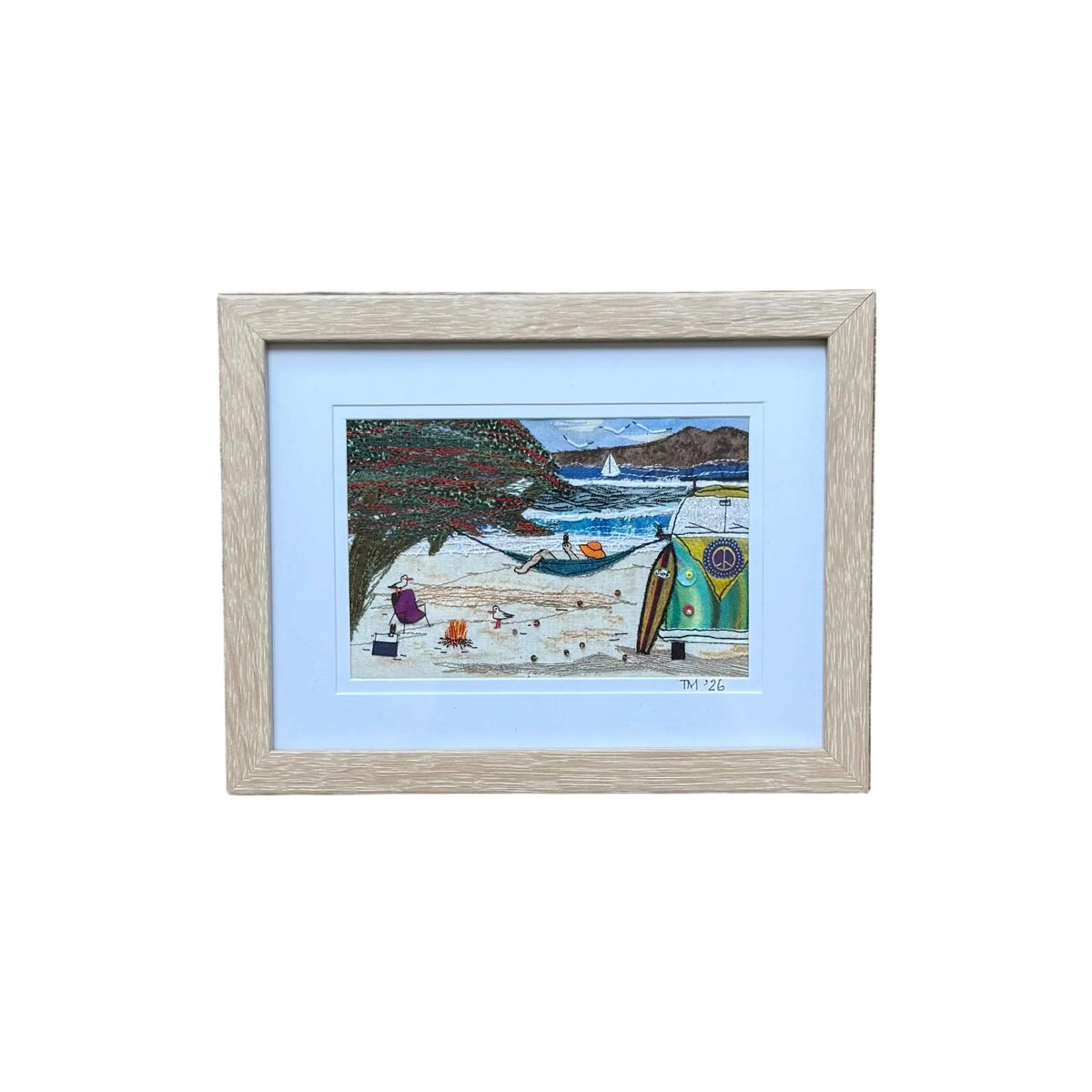 A colourful beach scene framed textile artwork with a hammock, beach tent, sailboat, trees, and a small campfire, presented on a white background.