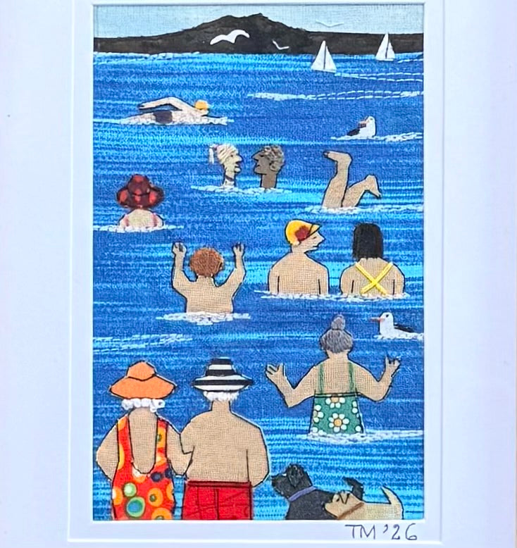 A textile & embroidered artwork depicting a whimsical seaside swimming scene. The artwork features stylized figures in the blue ocean, with a black mountain silhouette and white sailboats in the background.