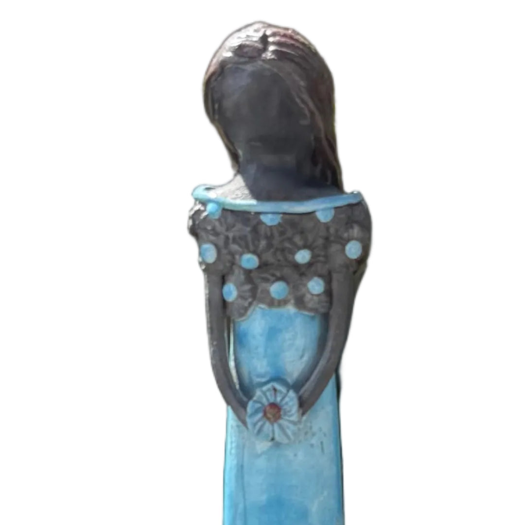 Close up view of a tall lady ceramic figure with an aqua glazed dress & dark floral bodice, holding an aqua flower against a white background.