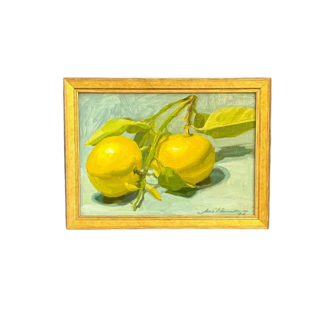 A small framed painting of two yellow grapefruit on a branch, placed on a white background.