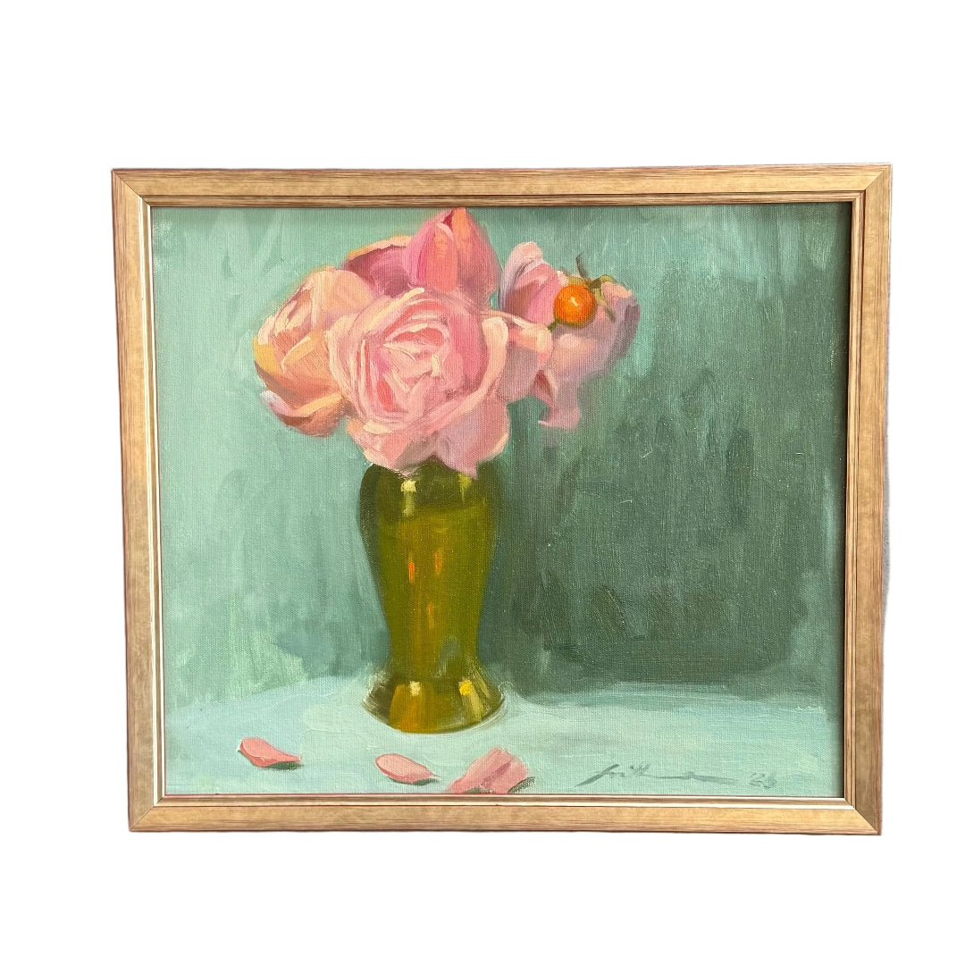 A framed still life painting of pink roses in a green-yellow vase, hung on a white wall.