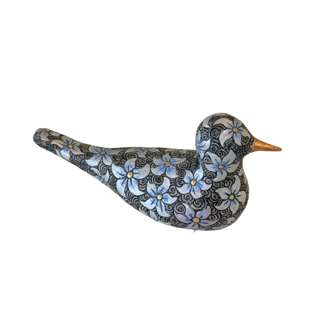 A decorative bird figurine with a black and white floral pattern and a metallic gold beak, resting on a plain white surface.