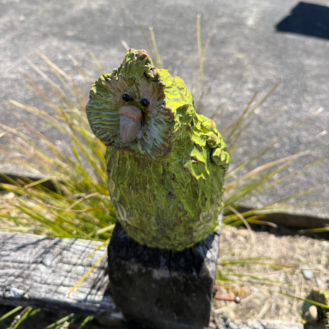 Green standing pottery Kakapo bird on a post in a garden.