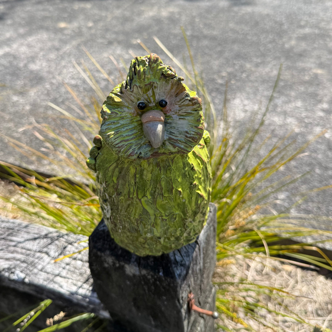 Green standing pottery Kakapo bird on a post in a garden.