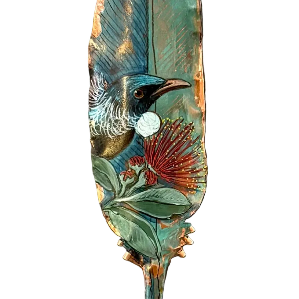 Close up od a decorative copper feather with a painted Tui bird on pohutakawa flower on a white background