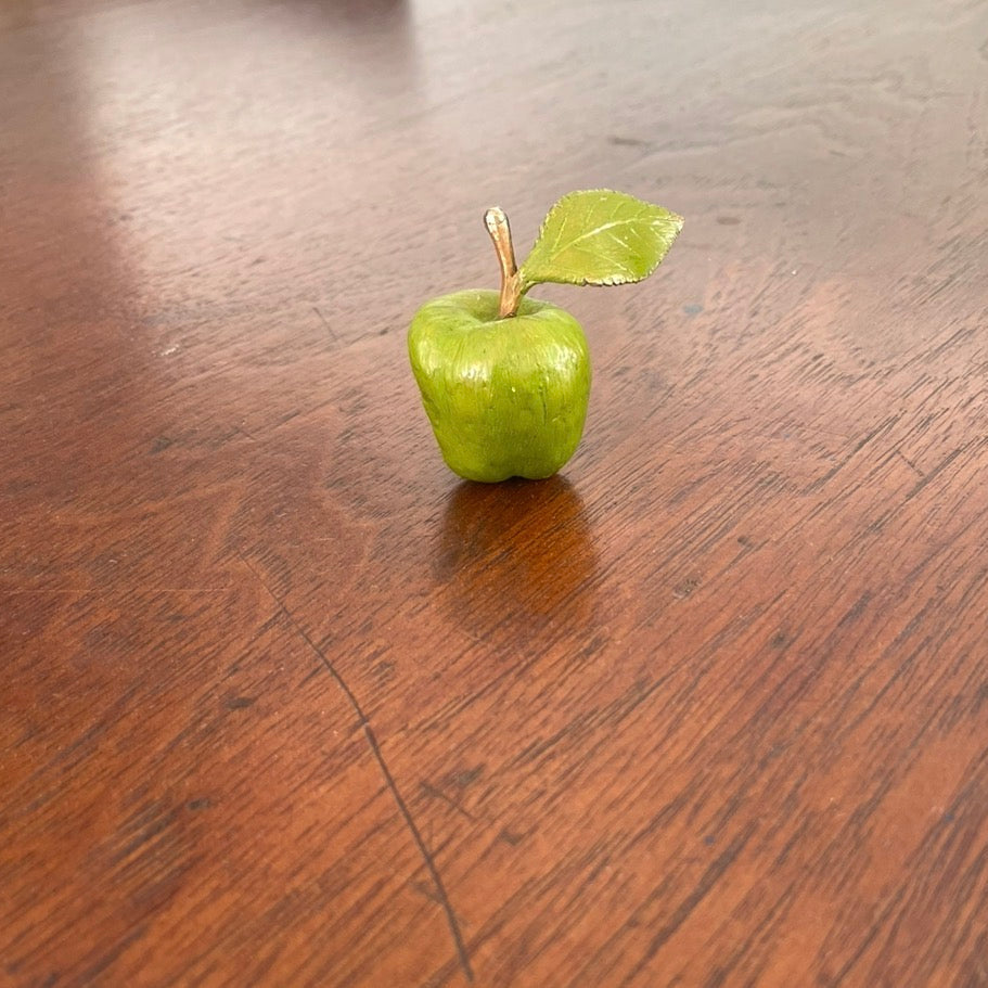 Painted bronze miniature green apple with leaf on a wooden table.