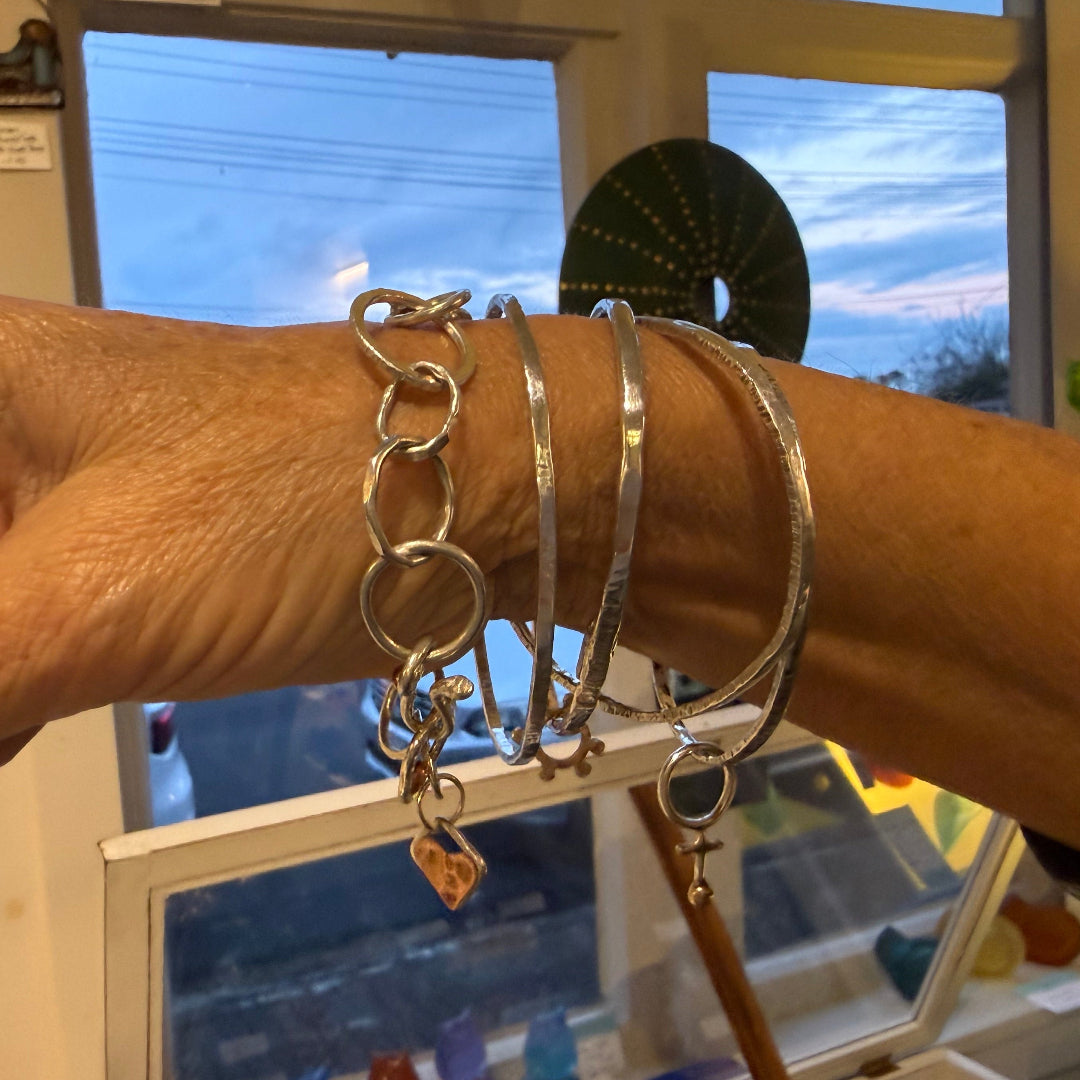 Person wearing multiple silver bracelets with a window and colorful objects in the background