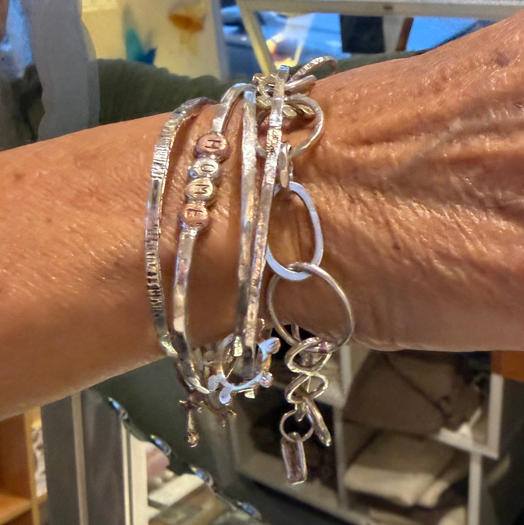 Close-up of a wrist wearing multiple silver bracelets with various designs.