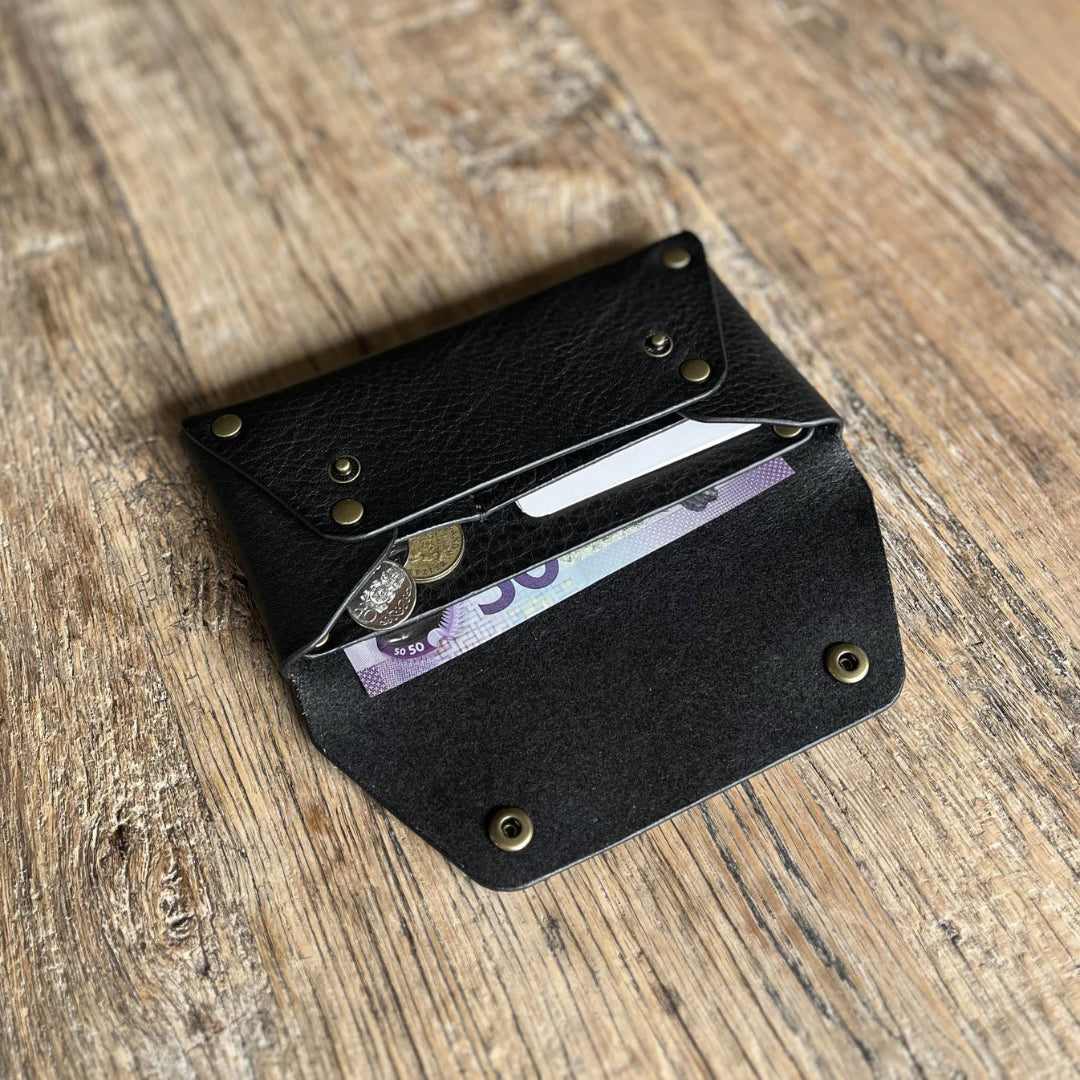 Black leather wallet with coins and a card on a wooden surface