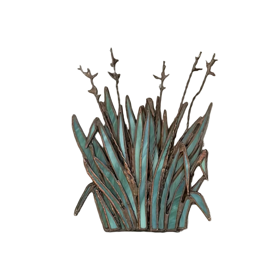 A decorative metal wall piece shaped like a clump of ornamental grass with a distressed turquoise and bronze finish, mounted on a white wall.