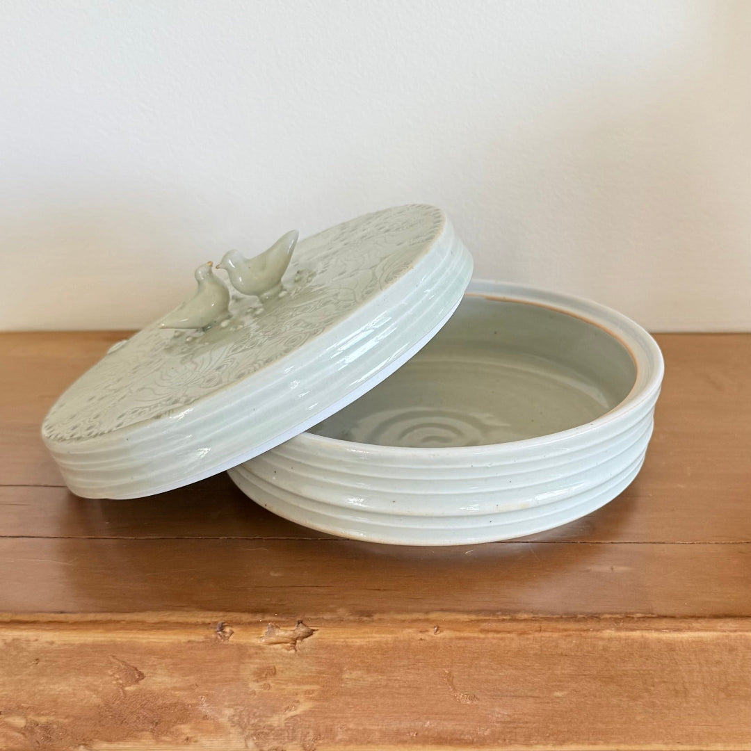 Ceramic dish with lid featuring bird designs on a wooden surface