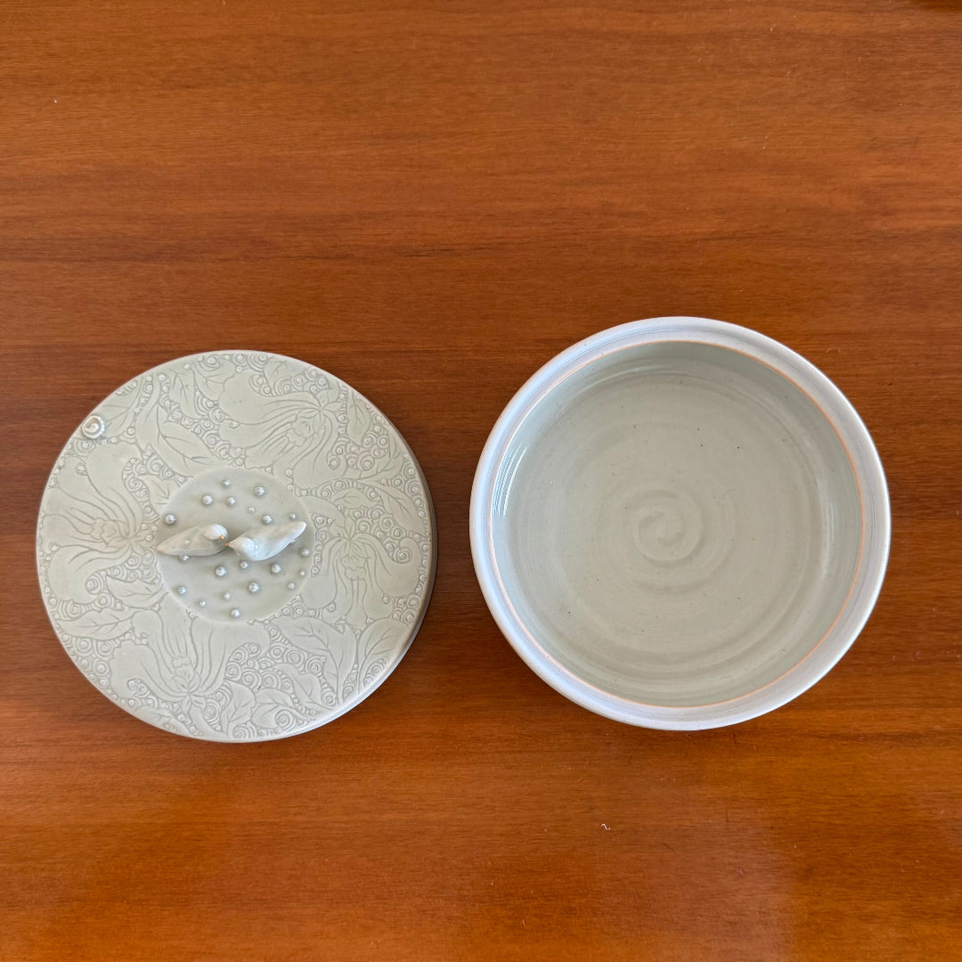 White ceramic lidded container with 2 birds on a wooden surface