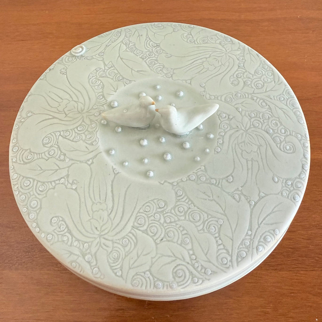 Ceramic keepsake box with embossed design and two small birds on a wooden surface