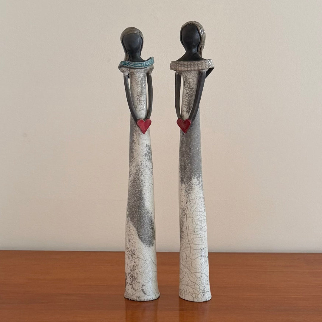 Two ceramic figures with cracked textures and red hearts on a wooden surface.