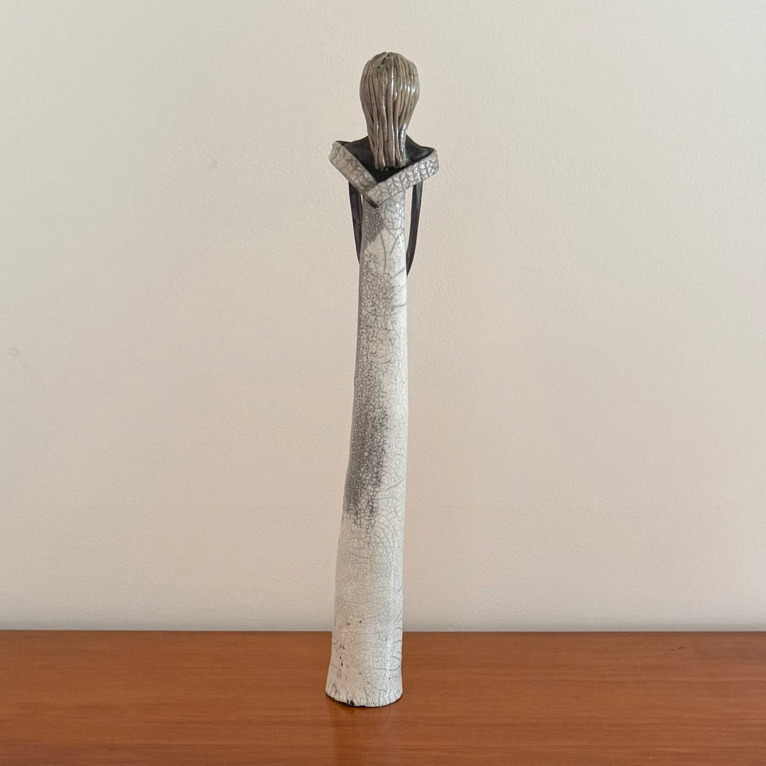 Ceramic figure with a textured design on a wooden surface and beige background