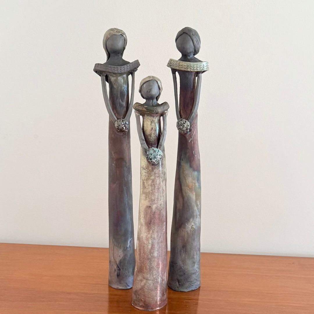 Three stylized human figure sculptures on a wooden surface with a plain background