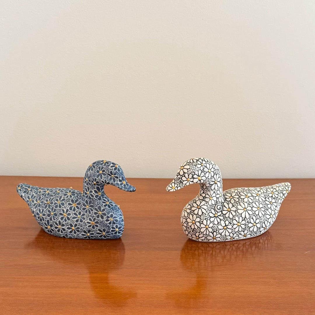 Two decorative duck figurines on a wooden surface with a neutral background