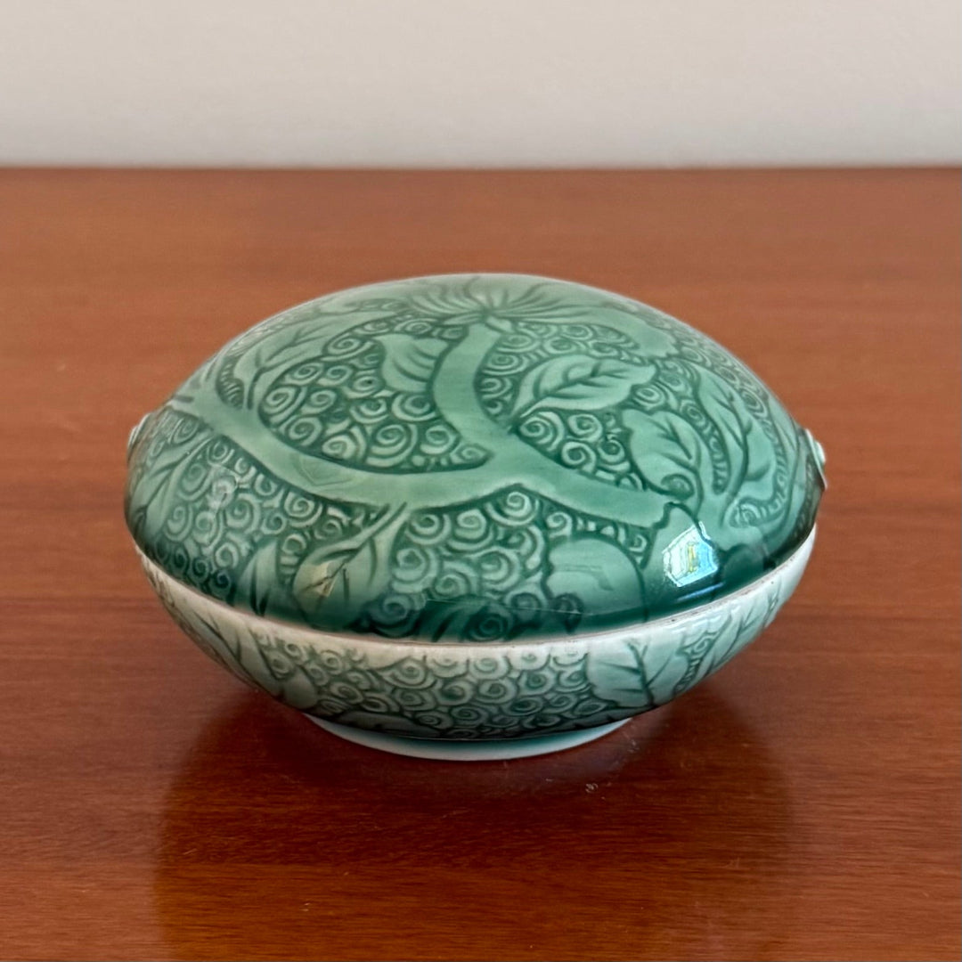 Green ceramic container with intricate patterns on a wooden surface
