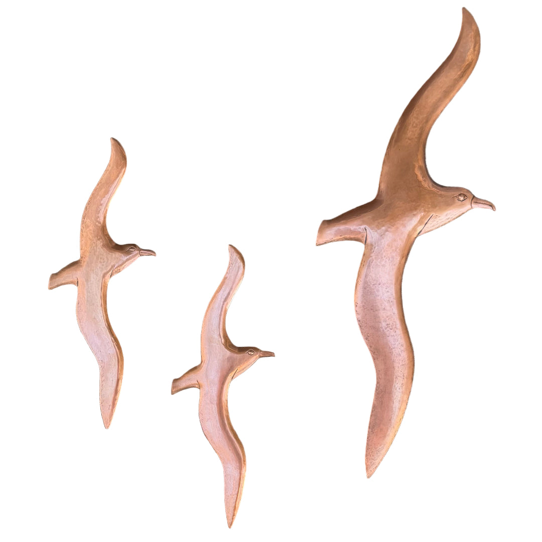 Three copper Albatross bird sculptures on a wooden surface