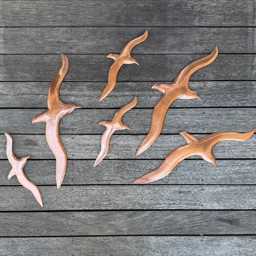 Flock of Copper Albatross sculptures on a wooden surface