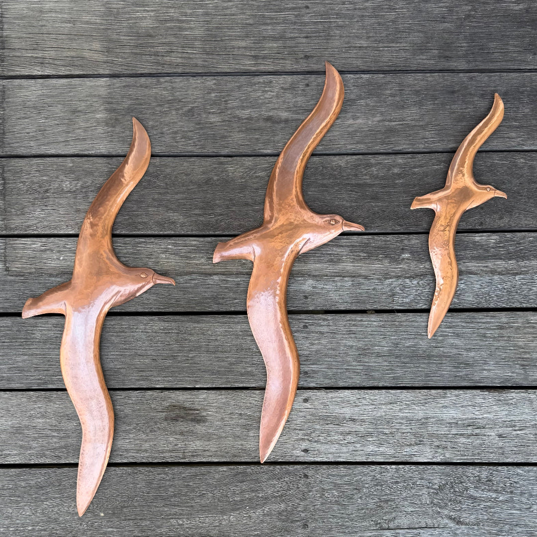 Three copper Albatross bird sculptures on a wooden surface