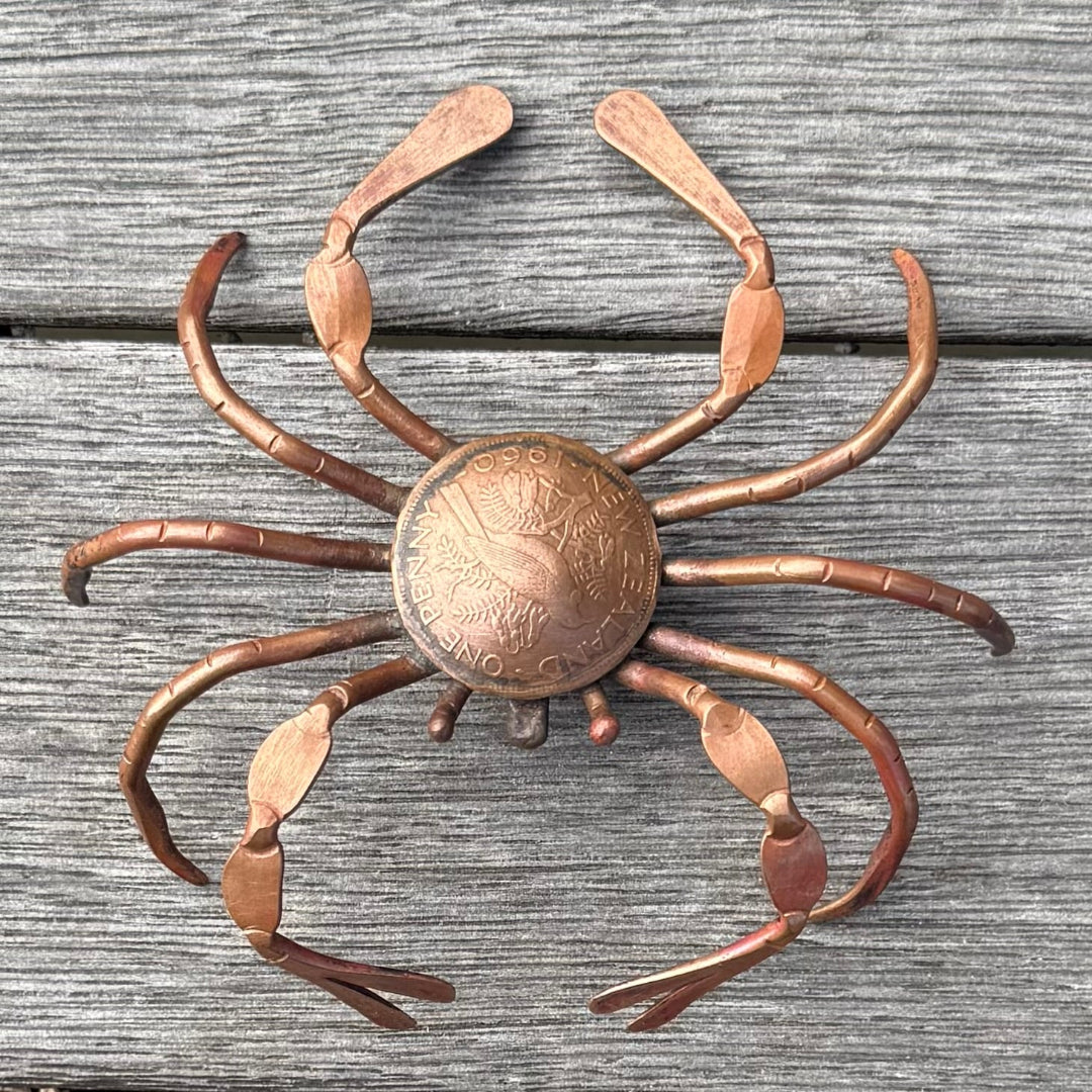 Copper crab wall art with a central coin on a wooden surface