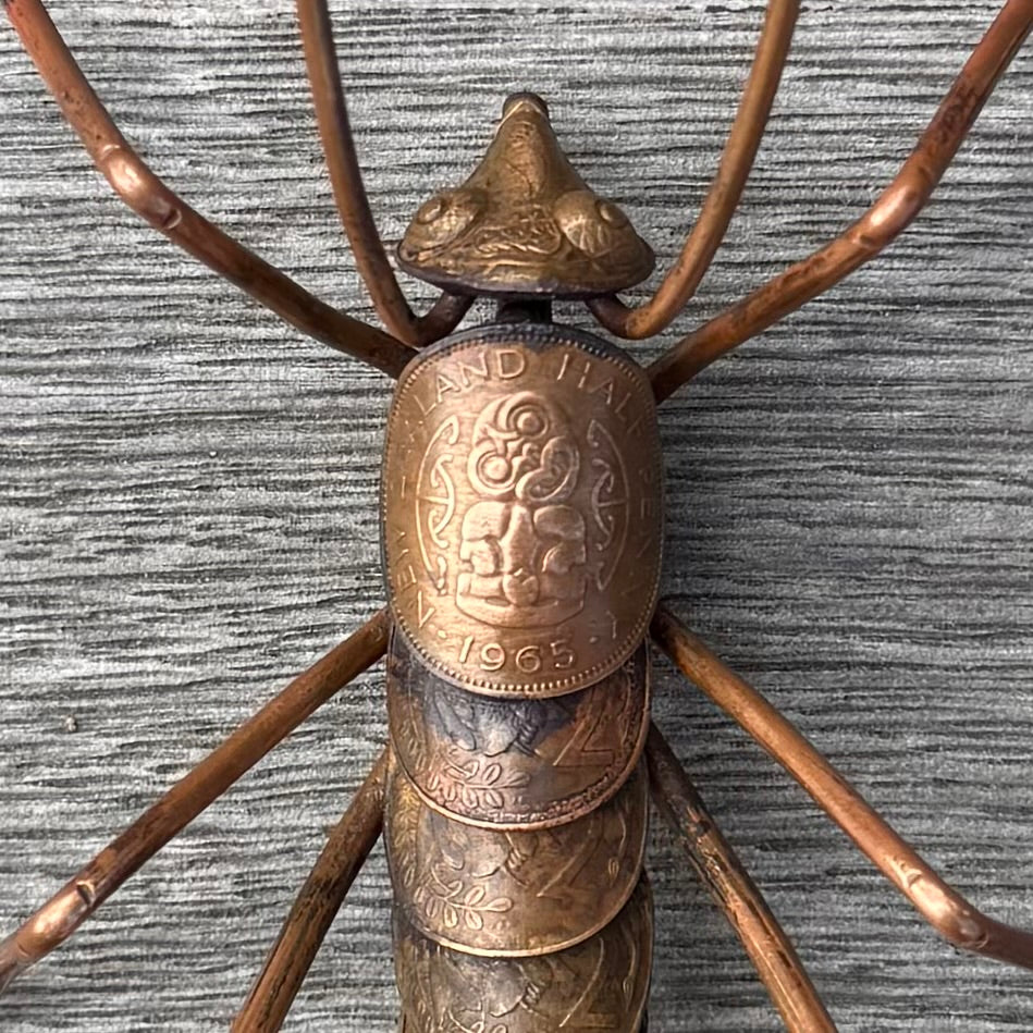 Copper Weta sculpture with a coin body on a wood surface