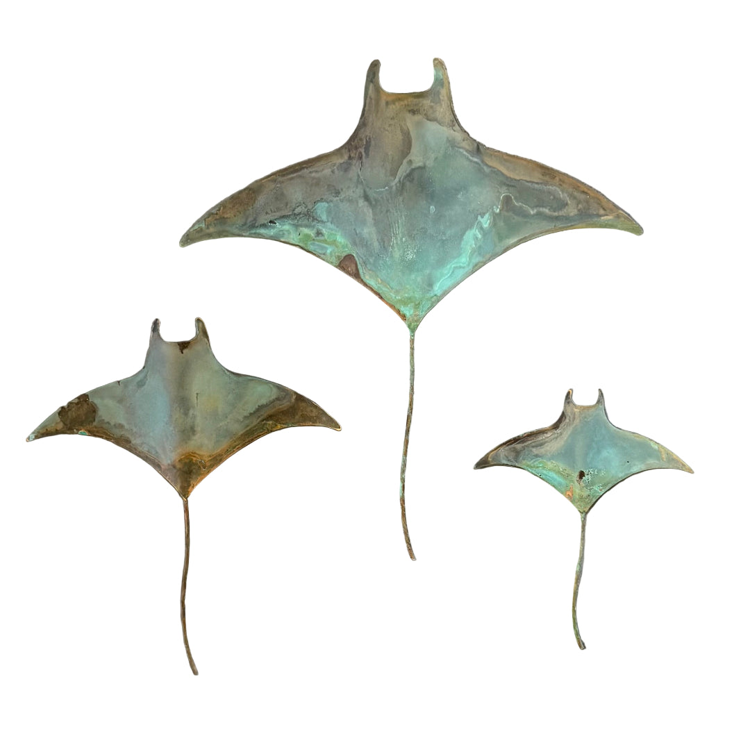 Three green patina'd copper manta rays on a white background