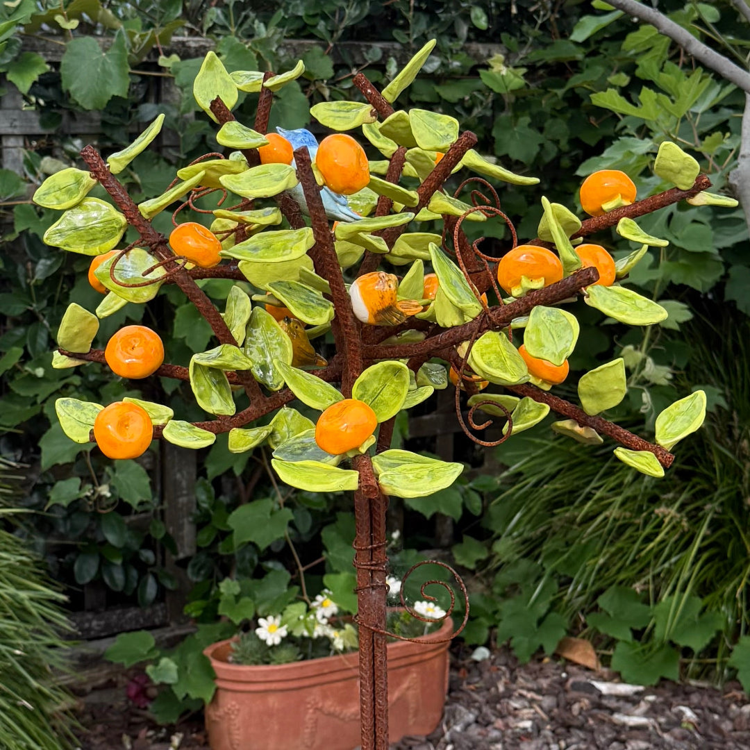 Decorative ceramic tree with orange mandarins and green leaves with a small bird in a garden setting