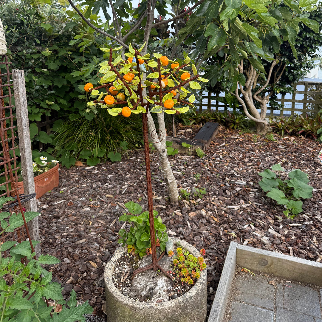 Decorative ceramic tree with orange mandarins and green leaves with a small bird in a garden setting