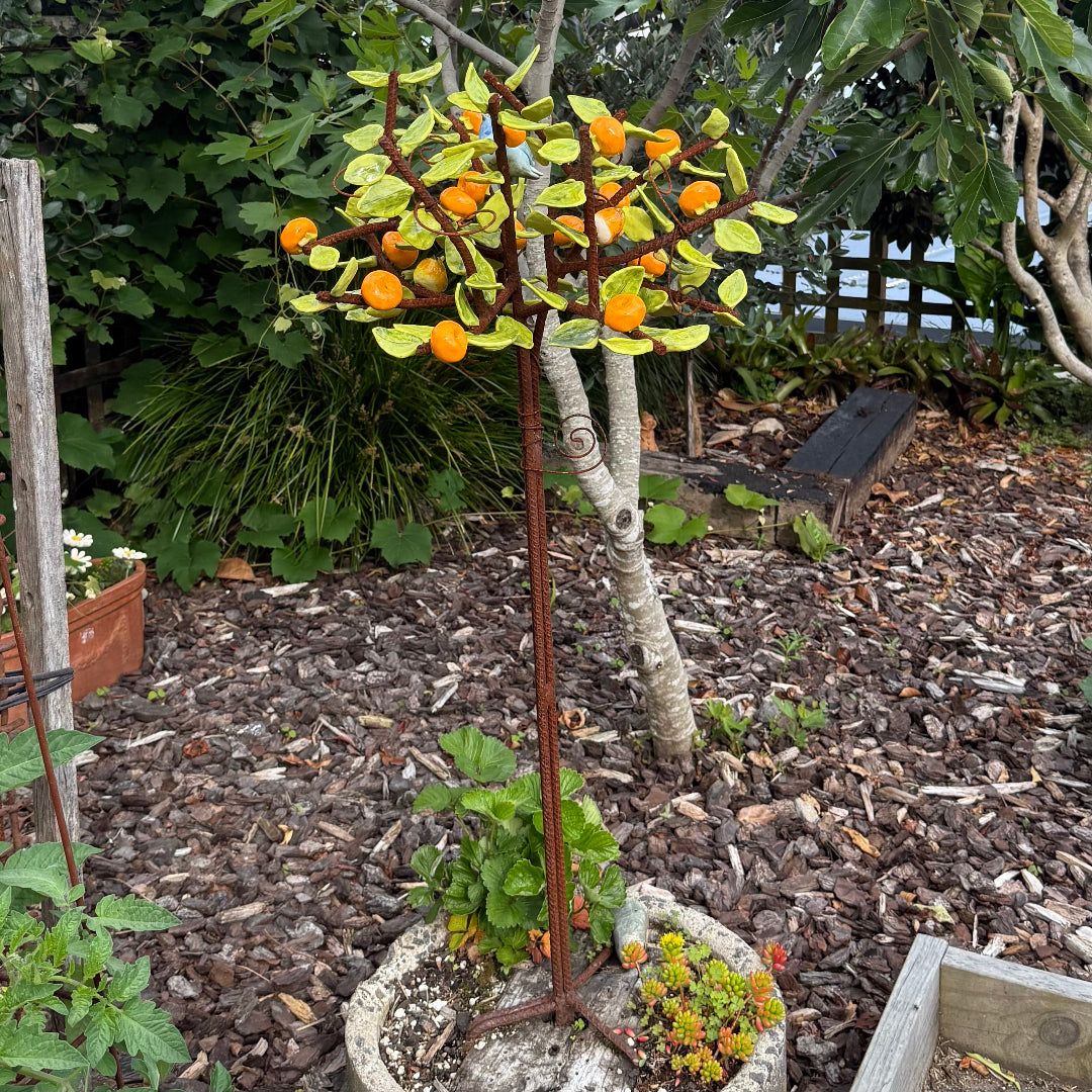 Small ceramic tree with orange mandarins in a garden setting