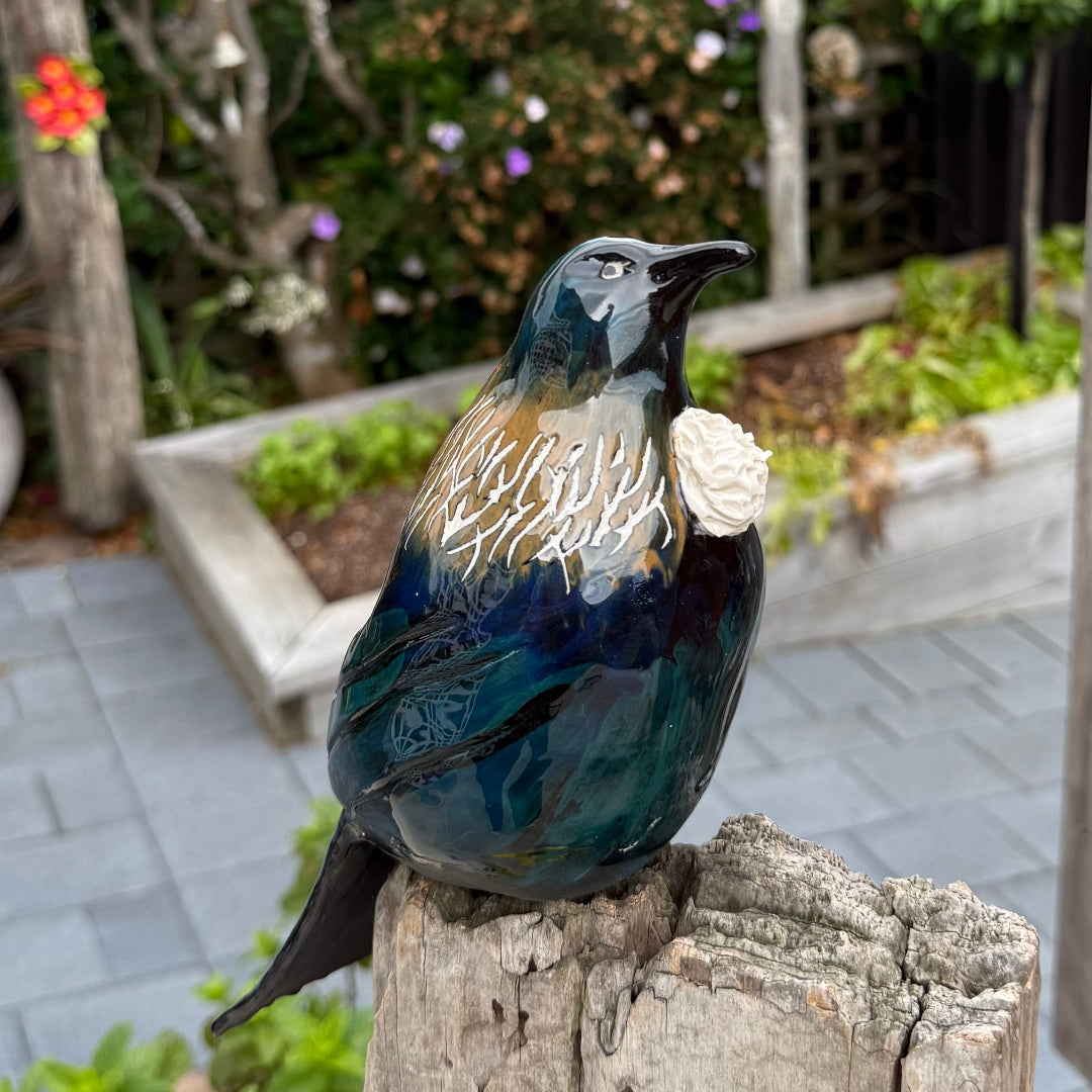 Ceramic Tui bird sculpture on a wooden post with a garden background