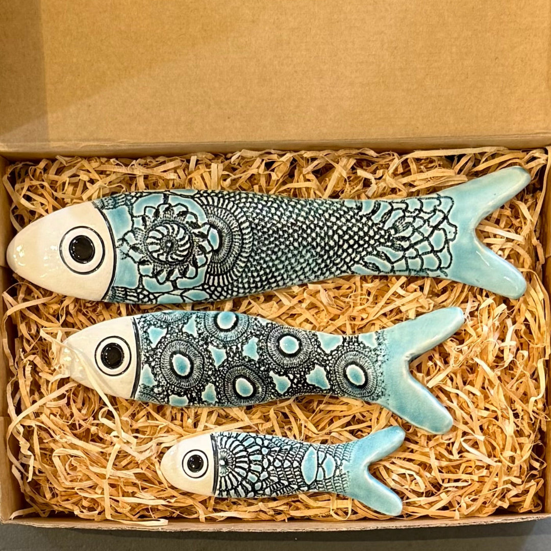 Decorative fish figurines with intricate patterns in a box with straw-like material.