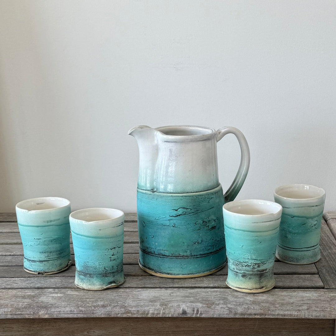 Set of ceramic tumblers with a pitcher on a wooden surface