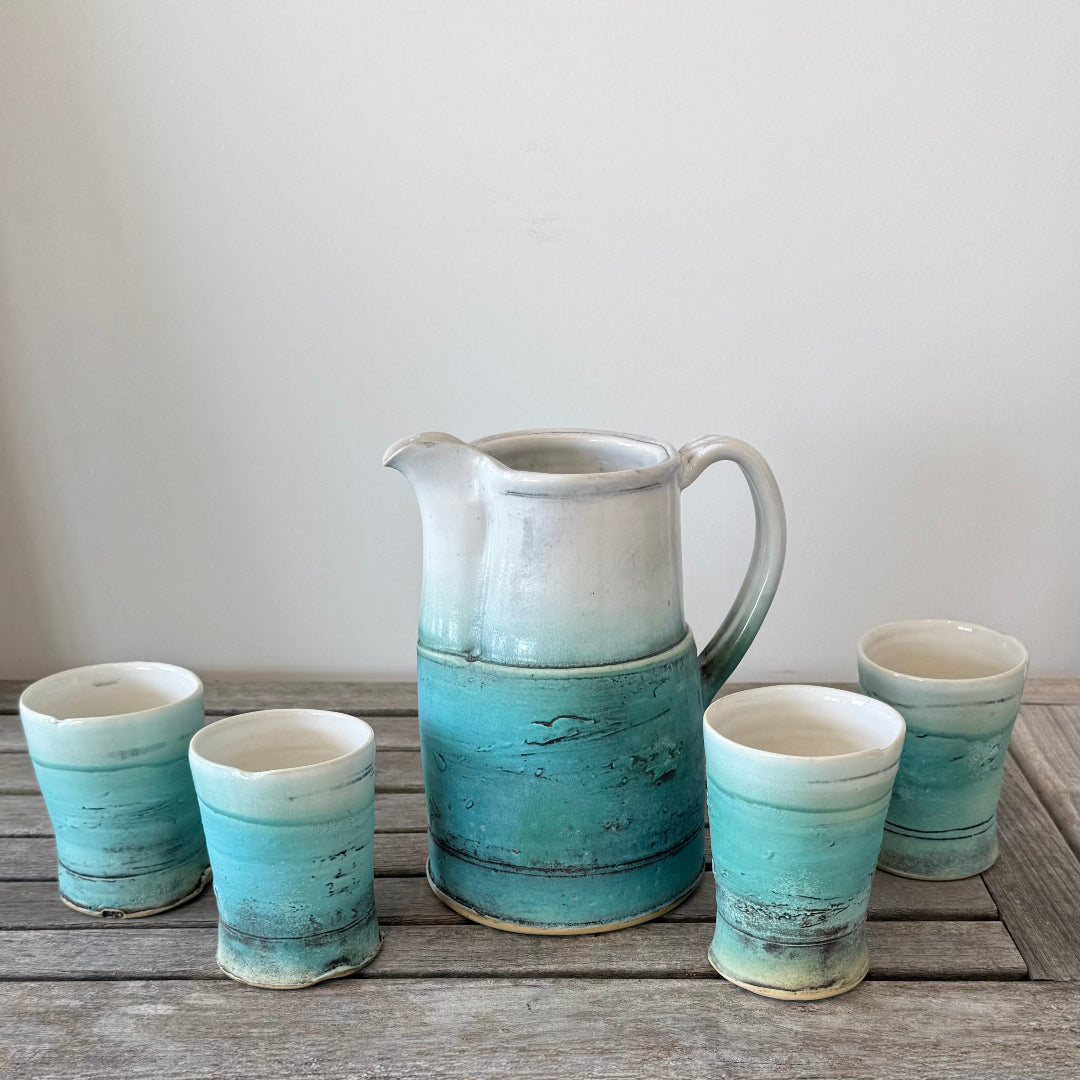 Set of ceramic tumblers with a pitcher on a wooden surface