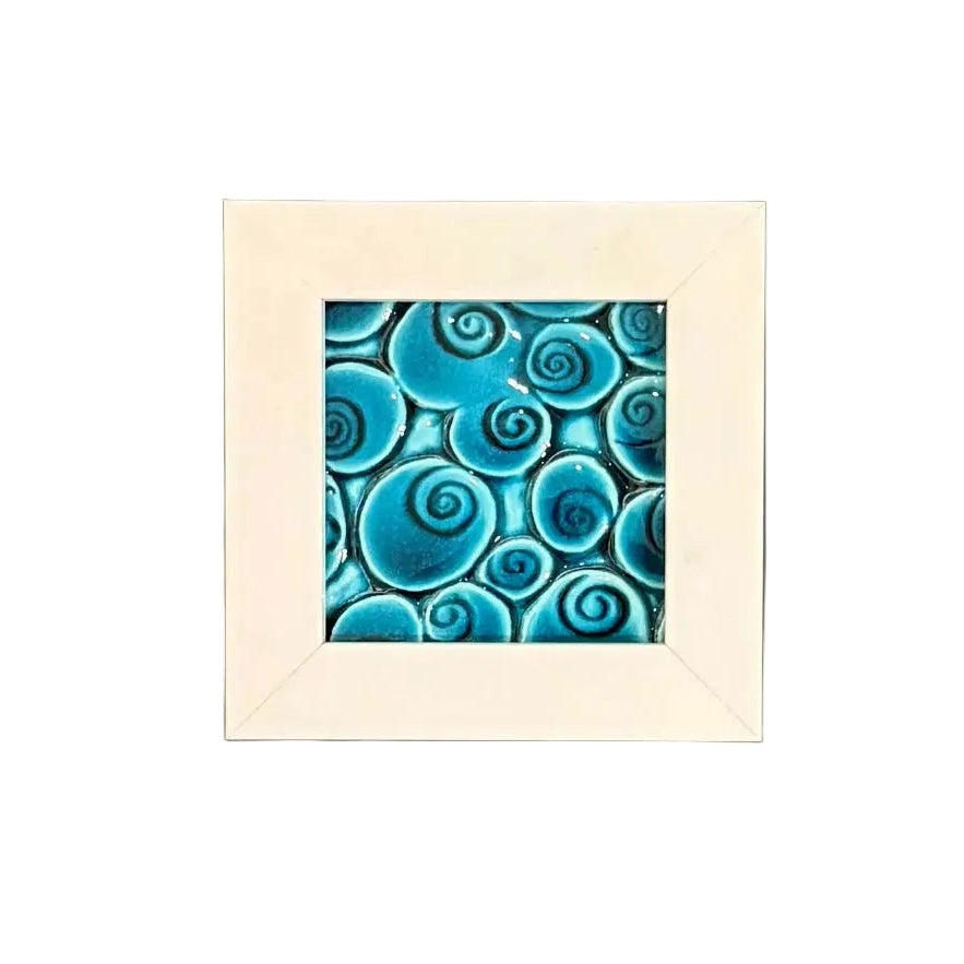 Framed porcelain tile with blue koru spiral pattern on a plain background