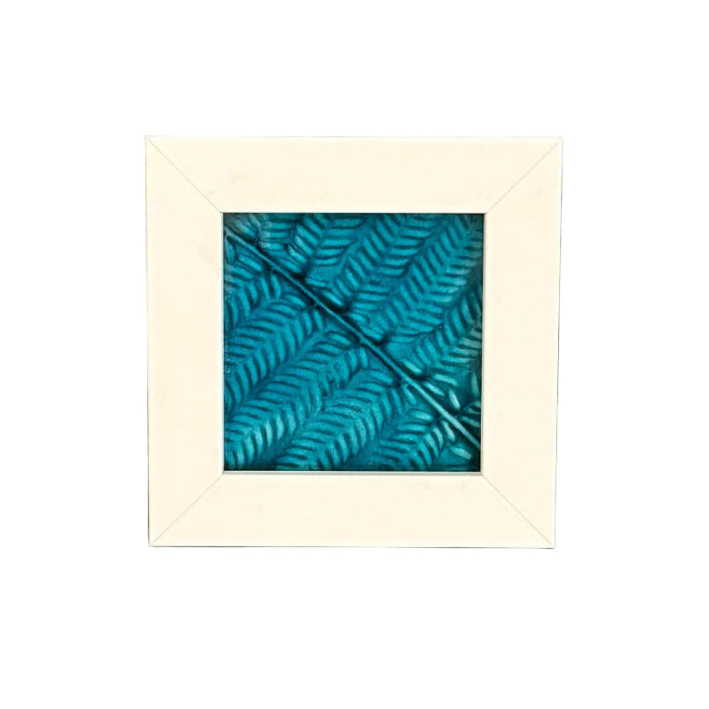 Framed artwork of a blue silver fern leaf on a white wall