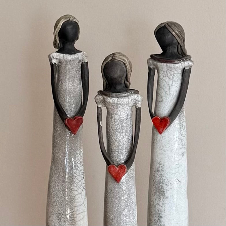 Three ceramic figures with cracked textures and red heart details on a beige background